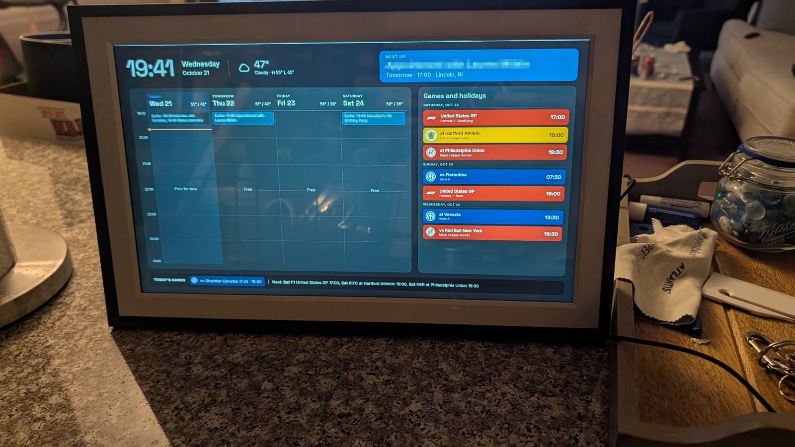 The finished calendar on a 15.6 inch photo frame sitting on a kitchen counter, showing the week on the left and color-coded games on the right